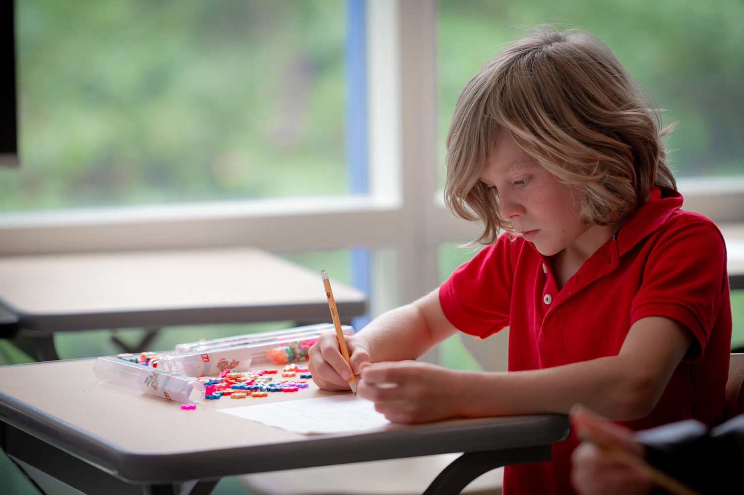 boy with blonde hair writing with a pencil
