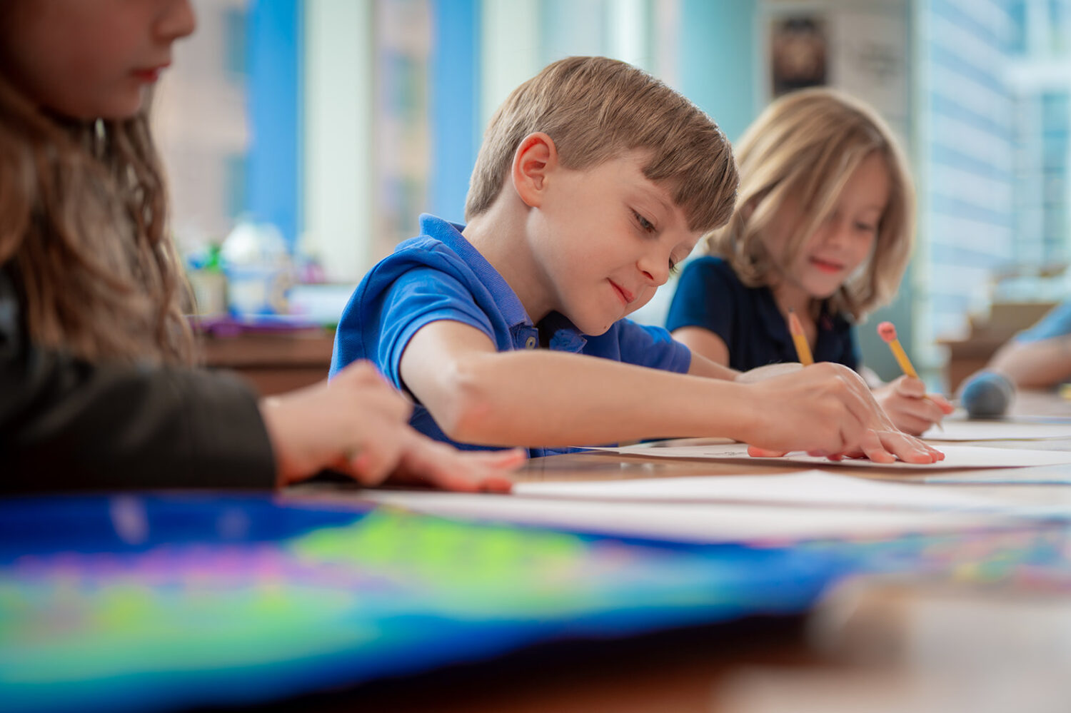 Boy writing at school next to two girls also working