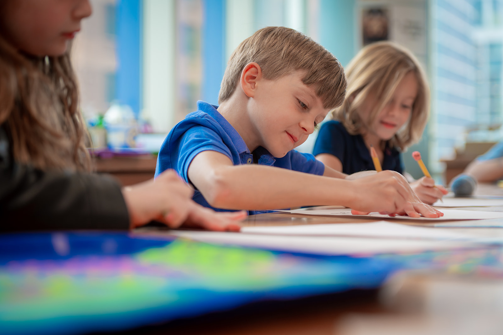 Boy writing at school next to two girls also working