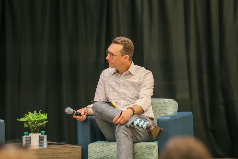 Man wearing glasses sitting on a chair holding microphone