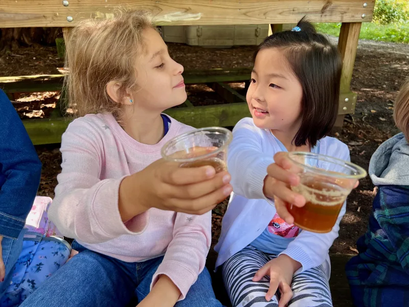Two young girls sitting outside drinking apple juice