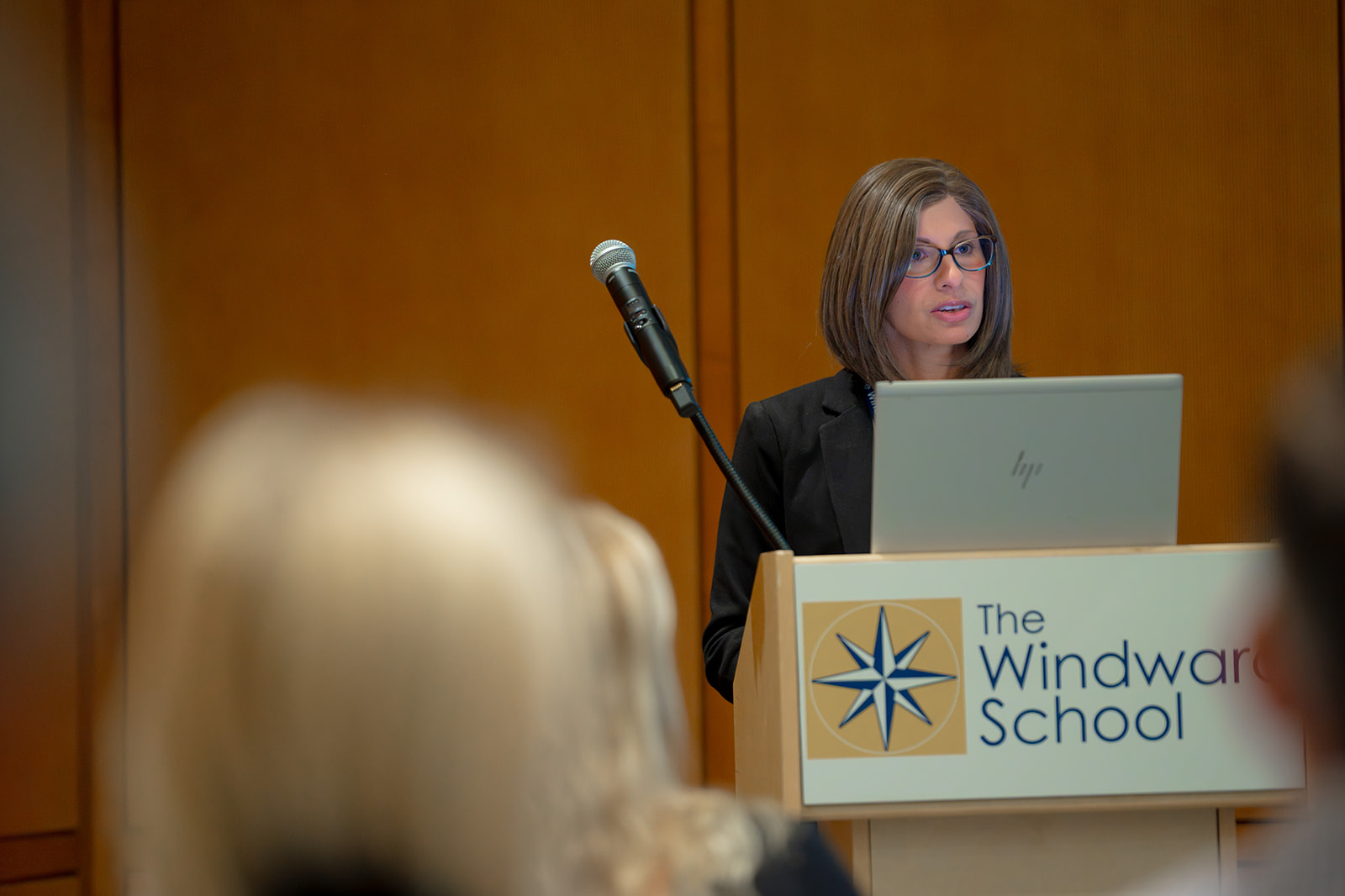 Women speaking on microphone at a podium in front of an audience